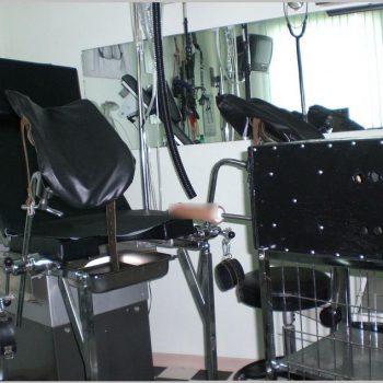 Im Klinikraum der Gynokologiestuhl und davor die Dildo-Maschine