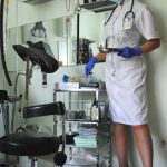 Ärztin Lind Dorn im Untersuchungsraum stehend vor und mit medizinischen Geräten im weißen Kittel